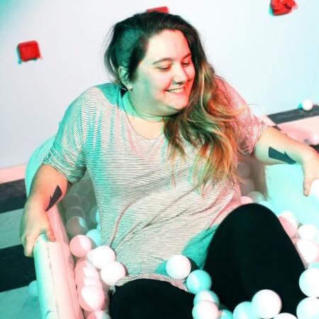 A picture of EmilyMadly sitting in a bathtub filled with large, white ping-pong balls.
